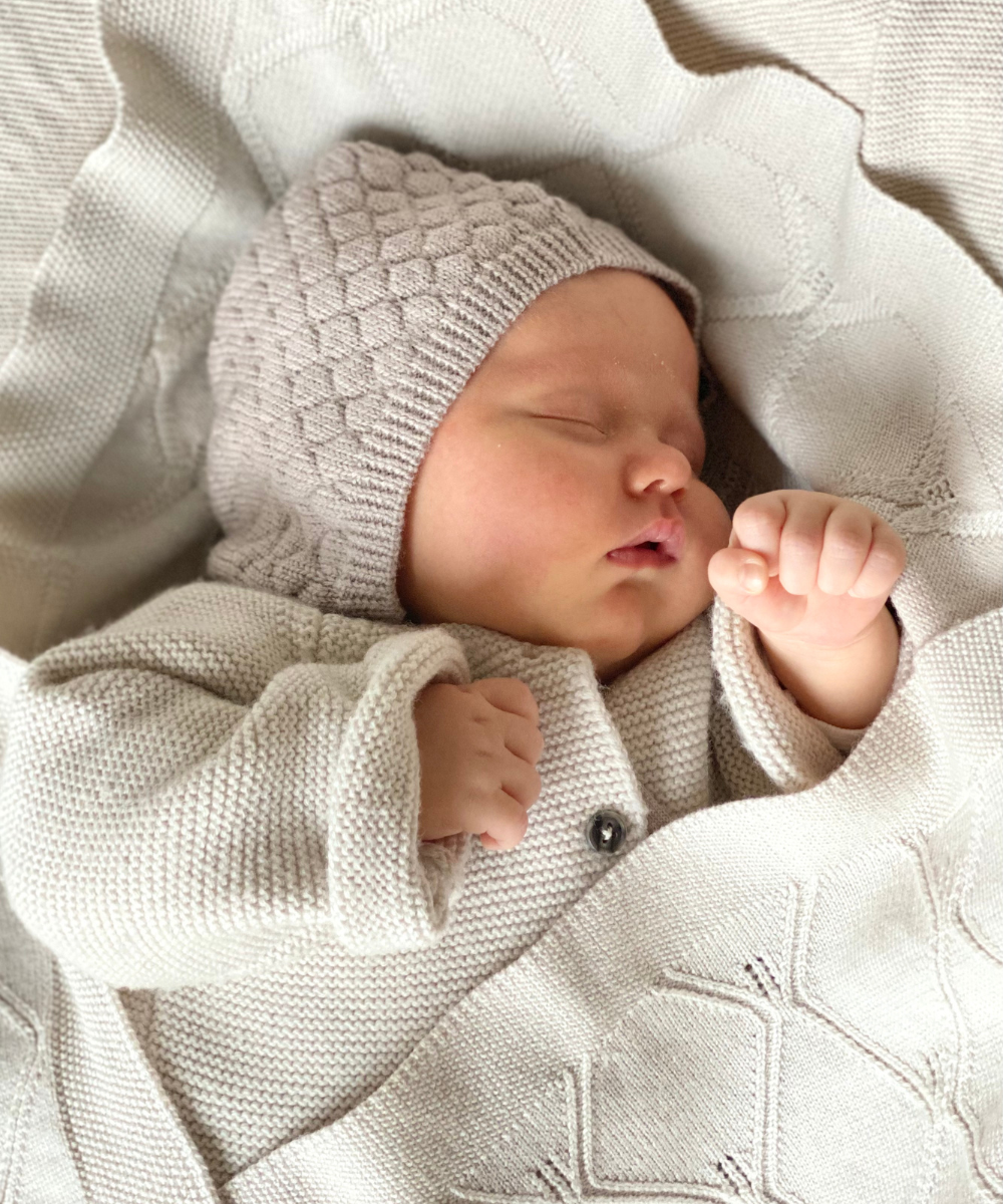 Kleines schlafendes Baby, das Lille Toni-Kleidung trägt und mit einer Decke zugedeckt ist